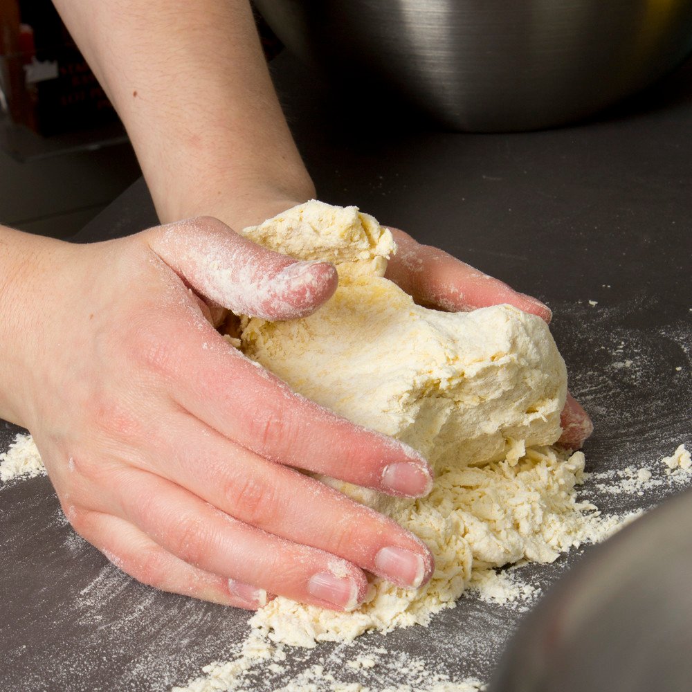 Mani che lavorano l'impasto con la farina